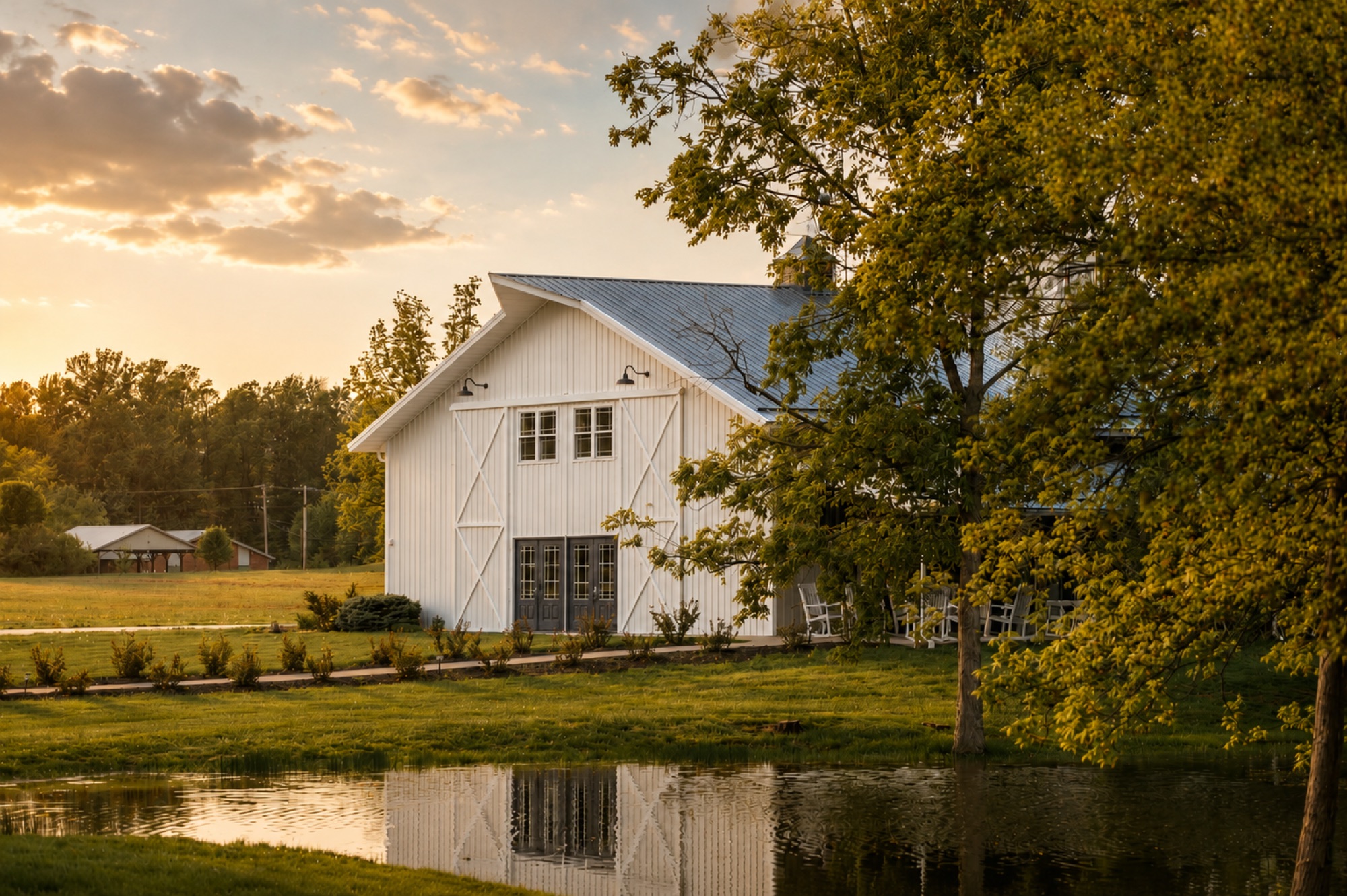 Rendering of the 2027 white barn exterior at Abram Farms, viewed across the pond at sunset